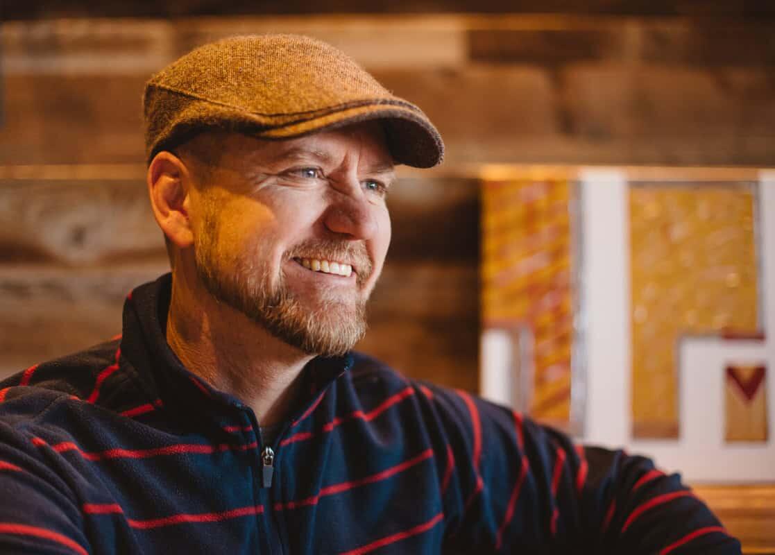Spencer Nix in a flat cap, smiling inside the taproom